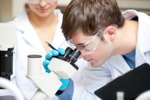 Caucasian male scientist holding pen and clipboard looking throu