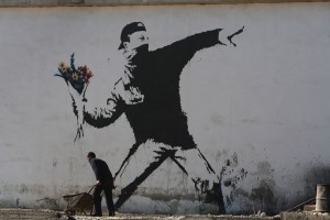 BETHLEHEM, WEST BANK - DECEMBER 05: A Palestinian labourer works under a large wall painting by elusive British graffiti artist Banksy December 5, 2007 on a building wall in the biblical city of Bethlehem in the West Bank. The Bristol-born artist has adorned Israel's West Bank separation barrier and Bethlehem walls with new images, including one of a dove wearing a flak jacket and a soldier being frisked by a young girl. His works, along with those of other international artists, are part of an exhibition called Santa's Ghetto. (Photo by David Silverman/Getty Images)